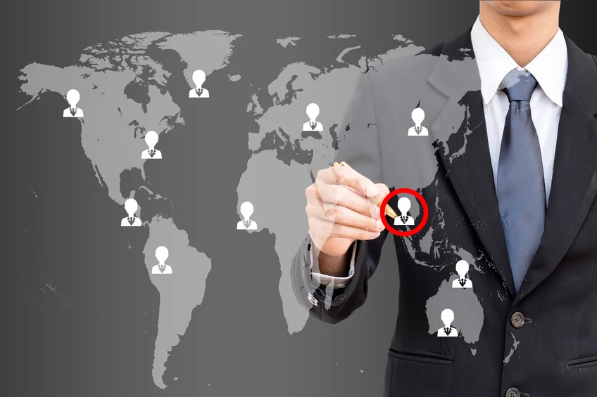 Businessman in a suit pointing to people icons spread across a world map